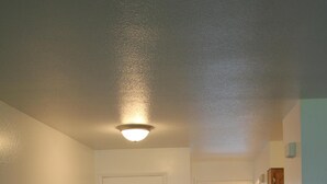 A compact room with a small dining table and chairs, a white door, a microwave, and a view of a balcony with a bed. - Corner Midtown Apartment (Anchorage)