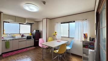 A compact kitchen with a dining area, featuring a sink, microwave, refrigerator, and a window with curtains.