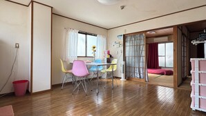 A room with wooden flooring, a dining table with colorful chairs, a small table with a vase of flowers, and a sliding door leading to another room. - N ° 5  CONDOMINIUM - Second Floor Corner Apartment; 2 BedRoom Japanese Style (Osaka-shi)