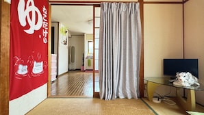 A traditional Japanese room with tatami flooring, a sliding door, a television, and a small table with a remote control. - N ° 5  CONDOMINIUM - Second Floor Corner Apartment; 2 BedRoom Japanese Style (Osaka-shi)