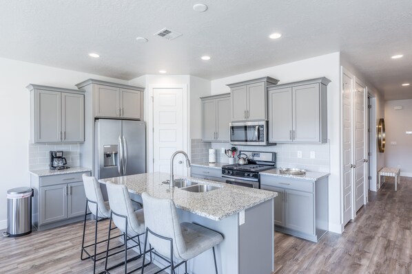 A modern kitchen with grey cabinets, stainless steel appliances, and a granite countertop island with bar stools. - 4BR on the 18th Green - Desert & Mountain Views (St. George)
