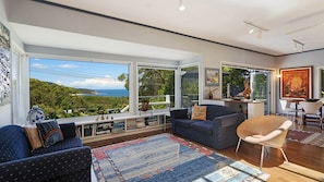 Uma sala de estar espaçosa com uma grande janela que oferece uma vista panorâmica do oceano e das colinas.