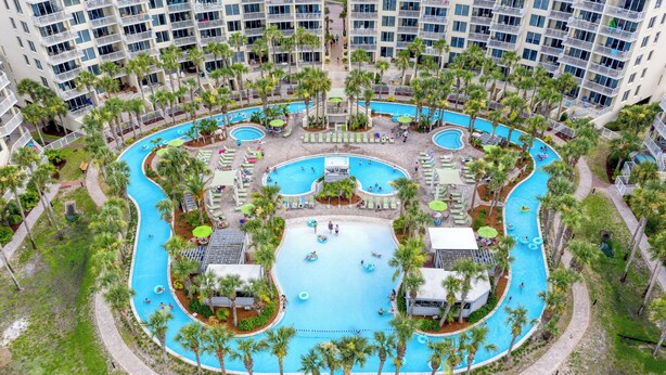 Un grand hôtel à plusieurs étages, doté d’une piscine centrale entourée de palmiers et de chaises longues.