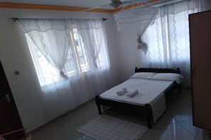 Cozy retreat with a comfortable bed, bedside table, and a window with sheer curtains.