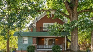Una casa a due piani con tetto verde, un balcone e un portico.