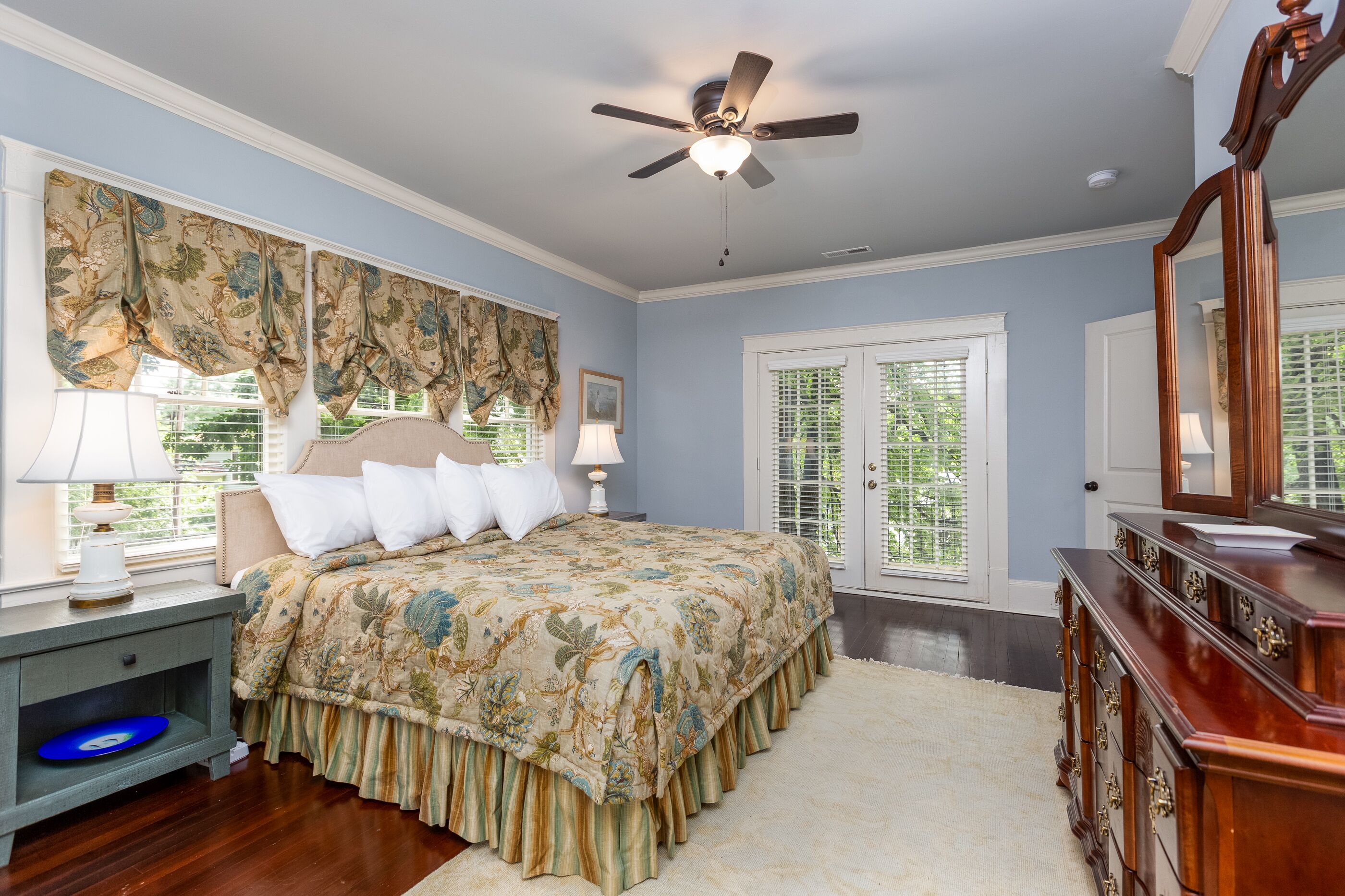 Une chambre à coucher comprenant un lit, une table de chevet, une commode et un ventilateur de plafond.