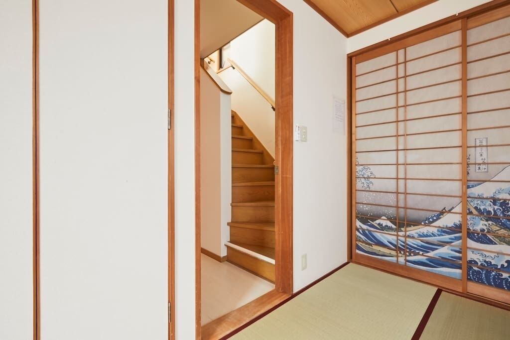 A traditional Japanese room with tatami flooring, a shoji screen with wave painting, and a wooden staircase.
