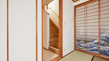 A traditional Japanese room with tatami flooring, a shoji screen with wave painting, and a wooden staircase.