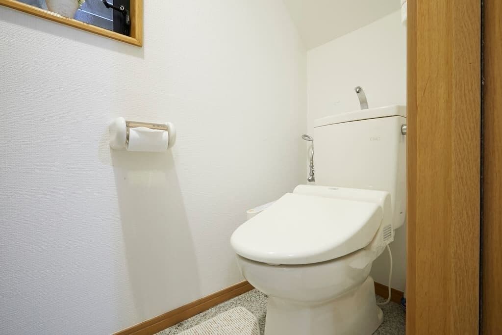 A small, clean bathroom with a toilet, a hand dryer, and a toilet paper holder on the wall.
