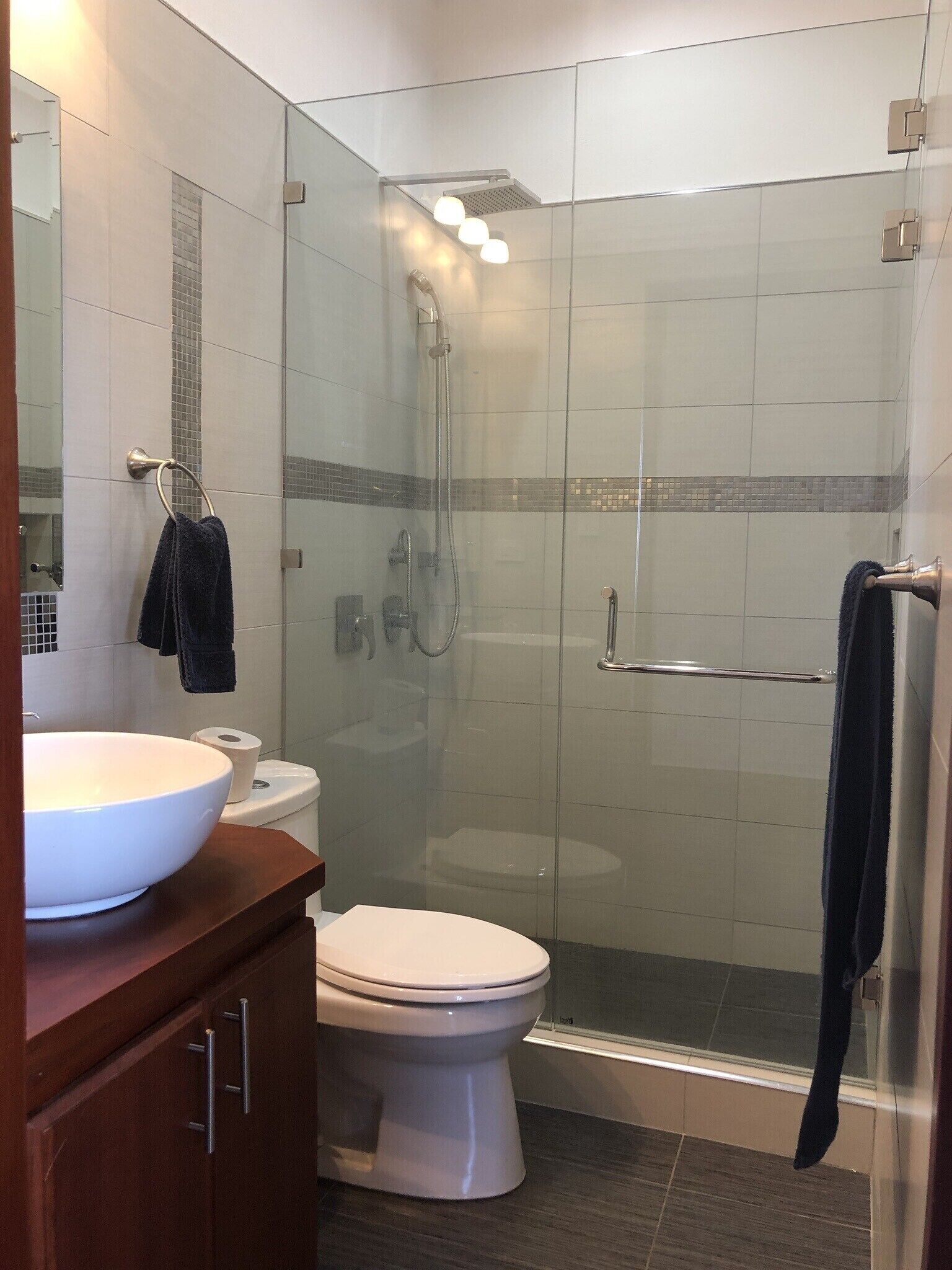 Een moderne badkamer met een douchecabine van glas, een wit wastafeltje en een toilet.
