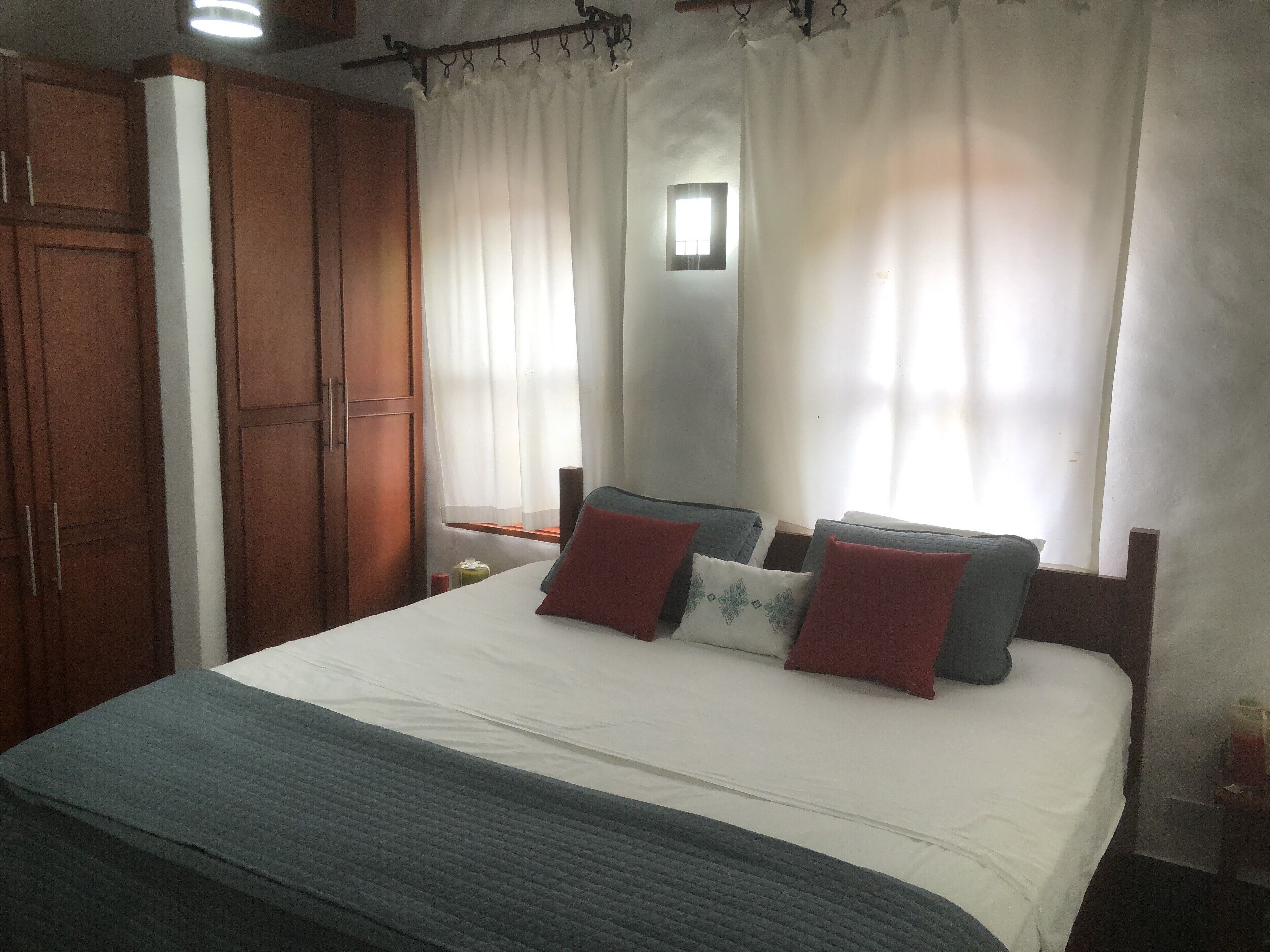 A bedroom with a bed, wooden wardrobe, and a window with curtains.