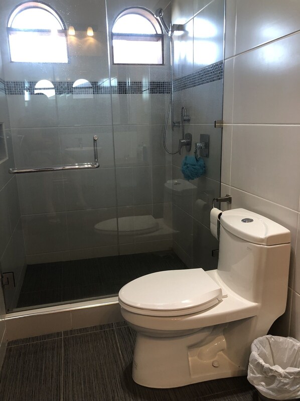 Een moderne badkamer met een douchecabine van glas, een toilet en een hygiëneschuimer.