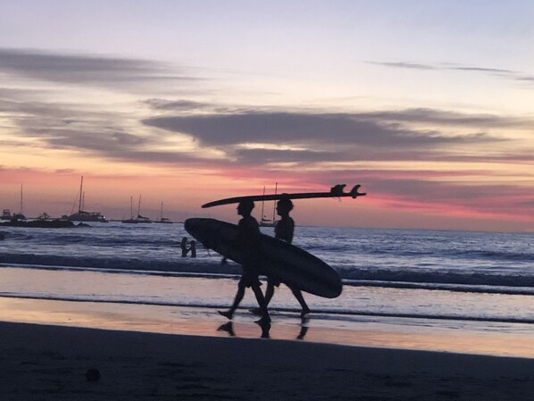 A beach scene with boats in the background and people walking with surfboards. - AMAZING OCEAN VIEWS AND SUNSETS Penthouse #1 (Tamarindo)