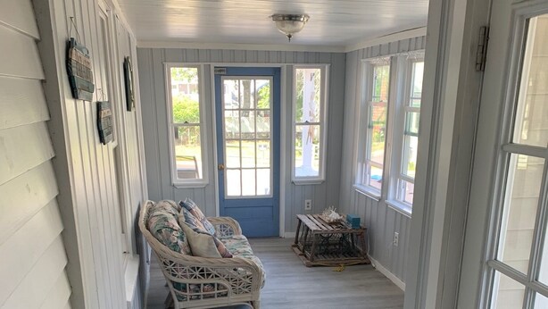 Une véranda couverte avec un canapé en osier, une petite table et une porte bleue.