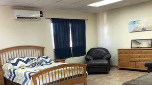 Ein Schlafzimmer mit einem hölzernen Bett, einem Schreibtisch, einem Stuhl, einer Kommode und einem Fenster mit Vorhängen.