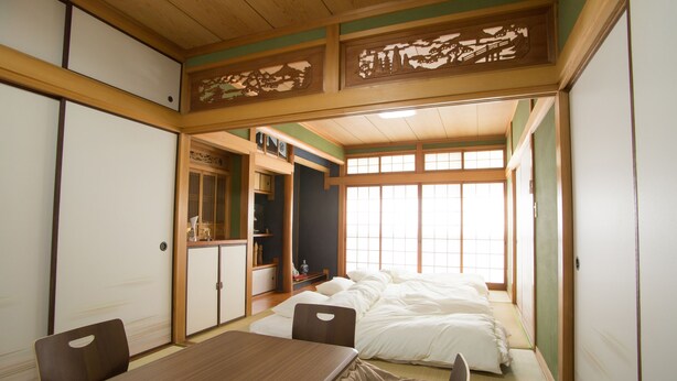 A traditional Japanese-style room with tatami flooring, a low table, and a bed with white bedding.