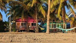 Una propiedad frente a la playa con un edificio rosa, un edificio verde y una hamaca en la arena.