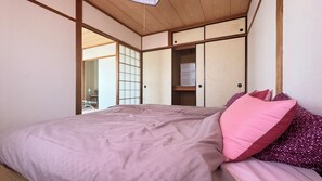 Een traditionele Japanse slaapkamer met een bed, glijdende deuren en uitzicht op een eetgedeelte.