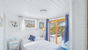 A bedroom with a bed, a nightstand, a lamp, a window with curtains, and a view of the outdoors.