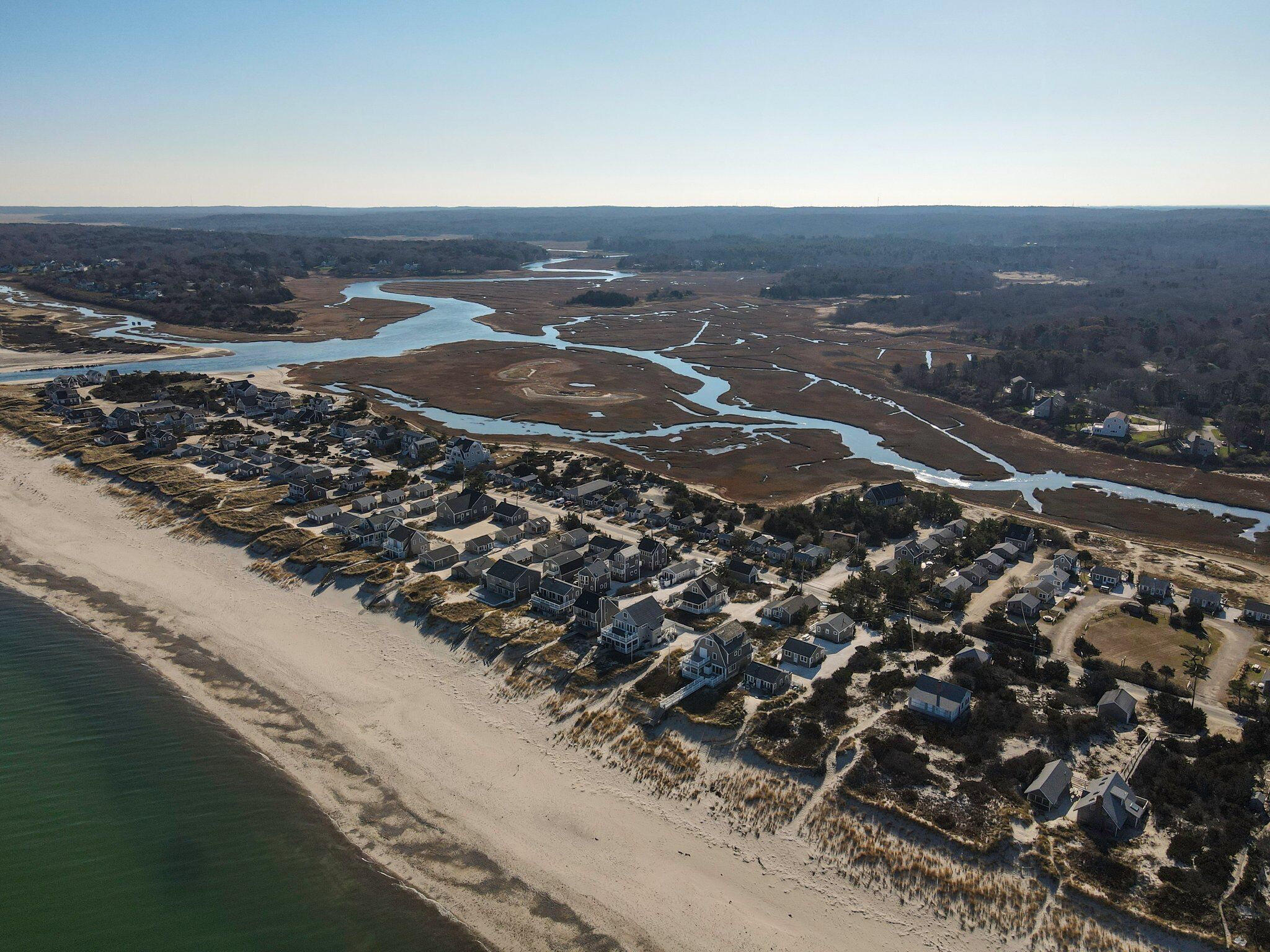 Eine Luftaufnahme einer Küstenwohngegend mit Häusern direkt am Strand und einem Fluss, der durch die Landschaft fließt.