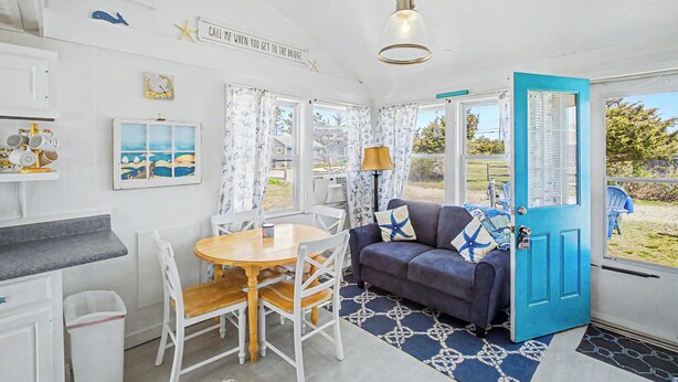 A room with a dining table, chairs, a sofa, a blue door, and a view of the outdoors.