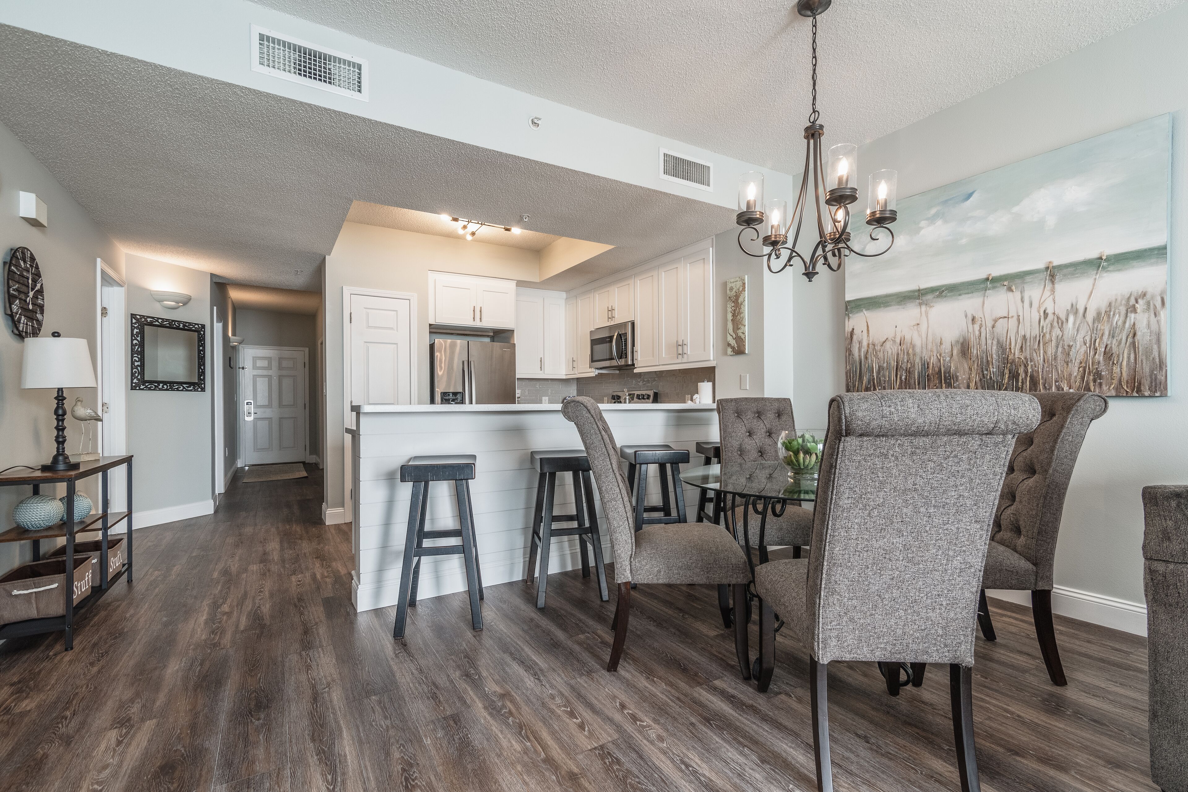 A modern kitchen with white cabinets, a central island with stools, and a dining area with upholstered chairs.