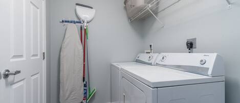 A laundry room with a washing machine, a drying rack, and a broom.