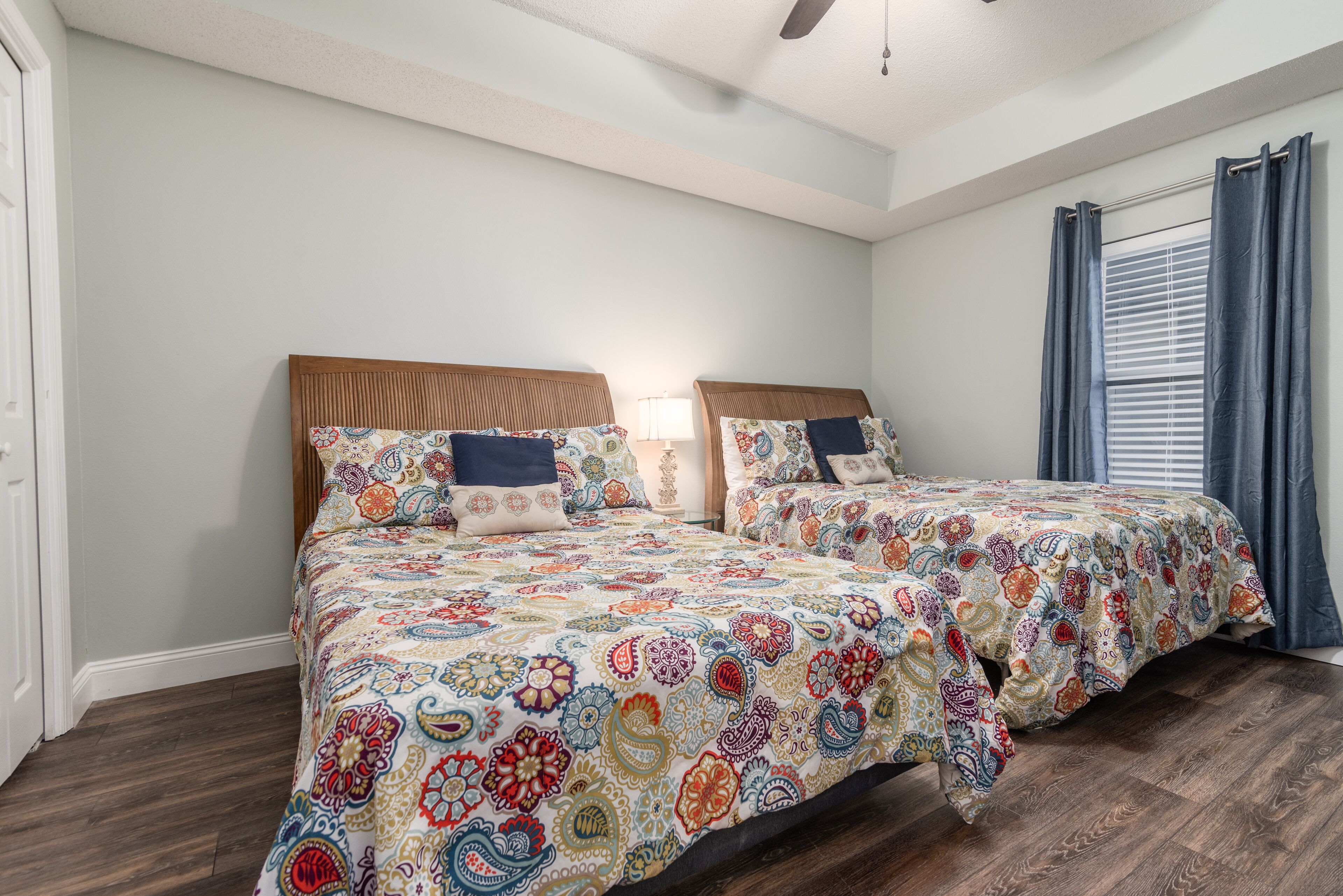 A bedroom with two beds, each with a patterned bedspread, wooden headboards, and a nightstand with a lamp.