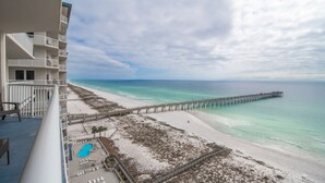 Une vue sur la plage depuis un balcon donnant sur une piscine, la plage et une jetée.