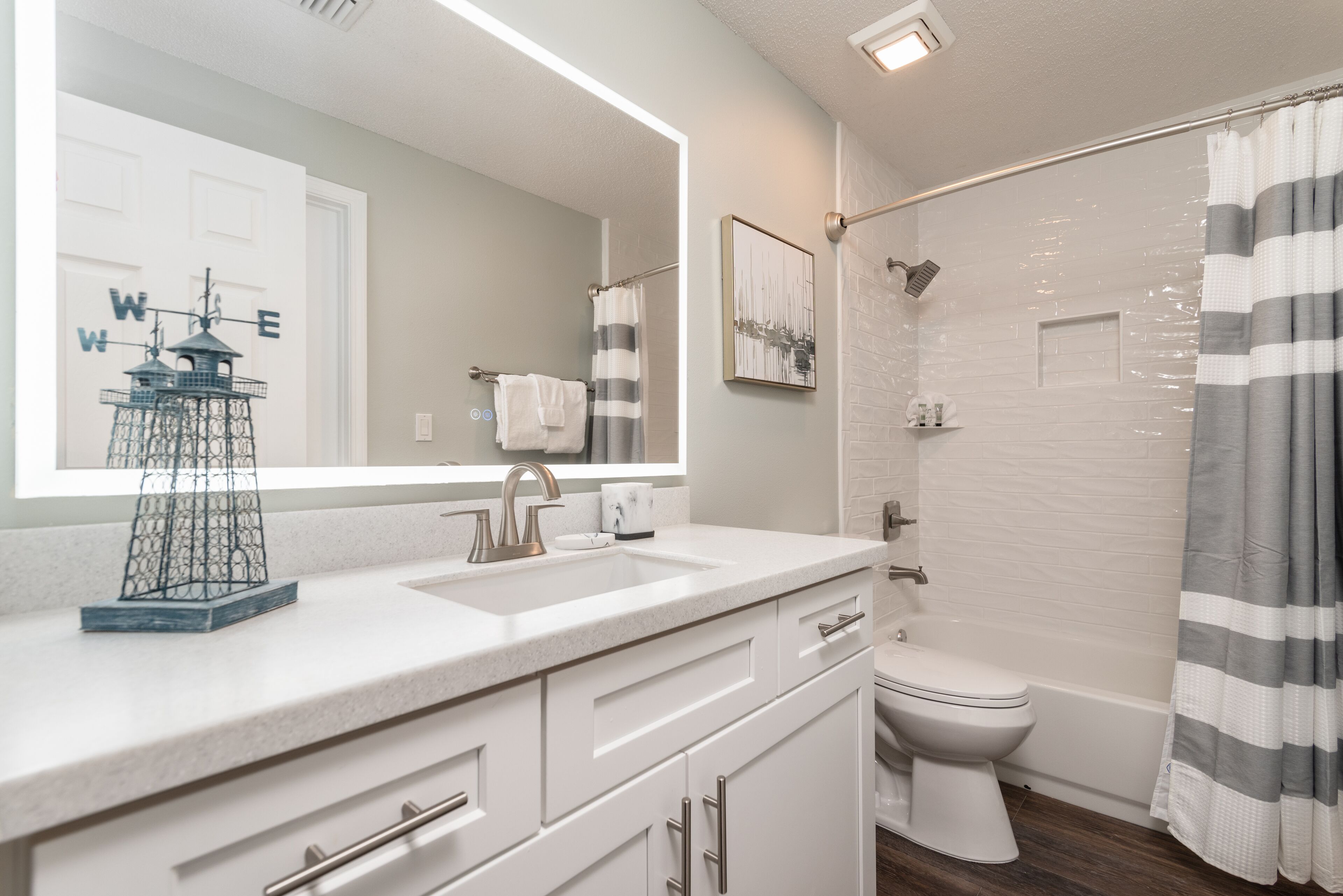 Une salle de bain avec un lavabo blanc, des toilettes et une douche. On y trouve un porte-serviettes et un tableau encadré au mur.