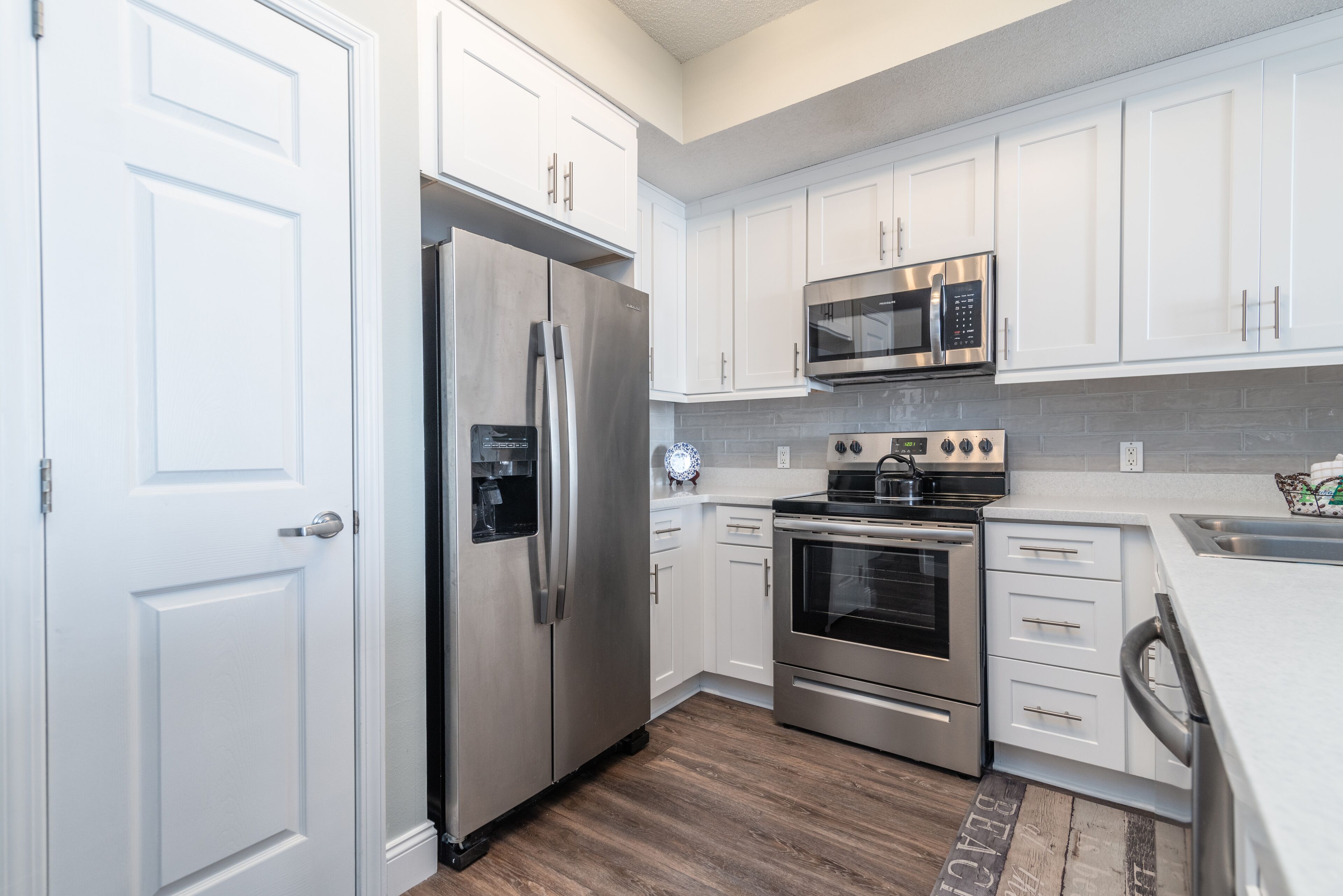 A modern kitchen with white cabinets, stainless steel appliances, and a wooden floor.