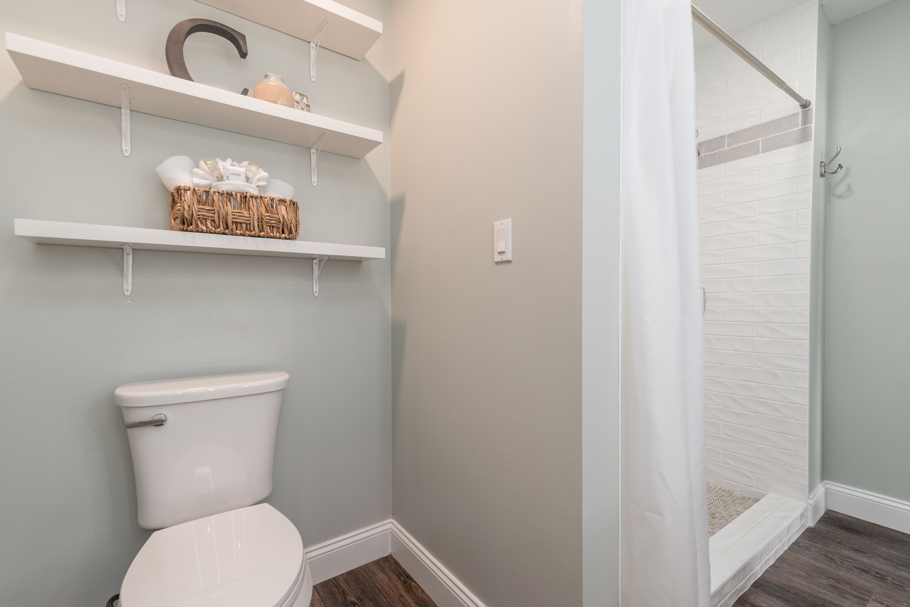 A bathroom with a toilet, white shelves with toiletries, and a shower area.