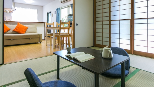 Una habitación tradicional japonesa con suelo de tatami, una mesita con un hervidor y un sofá con cojines naranjas.