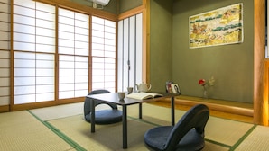 Una habitación con esteras de tatami, una mesa baja, dos cojines, un juego de té y un cuadro en la pared.