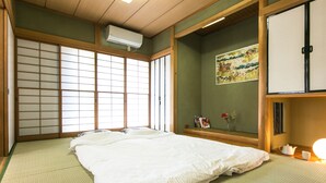 Una habitación japonesa tradicional con suelo de tatami, una cama grande, puertas correderas shoji y una pequeña estantería con libros y un jarrón.