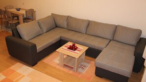 Ein modernes Wohnzimmer mit einer grauen Eckcouch, einem kleinen Holztisch und einem Essbereich mit Tisch und Stühlen.