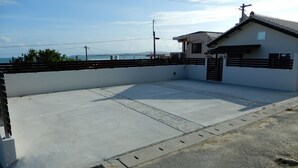 Eine Dachterrasse mit Betonboden, einem Metallzaun und einem kleinen Gebäude mit dunklem Dach.