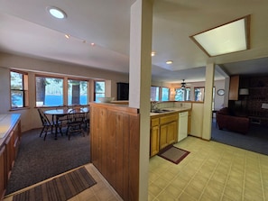 Una cocina con alacenas de madera, una zona de comedor con mesa y sillas, y ventanas grandes.