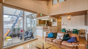 A modern interior with a glass wall, a sofa with decorative pillows, a dining area, and a kitchen. - Large city villa near Osaka Castle 5 min (Ōsaka-shi)