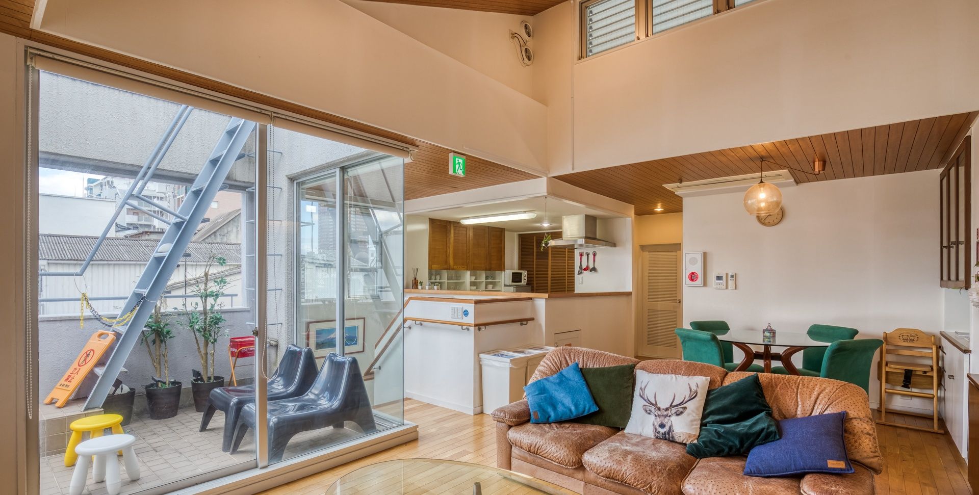 A modern interior with a glass wall, a sofa with decorative pillows, a dining area, and a kitchen.