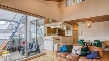 A modern interior with a glass wall, a sofa with decorative pillows, a dining area, and a kitchen.