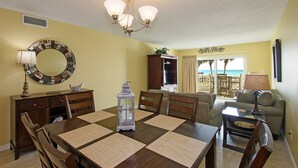 Un comedor con una mesa de madera, sillas, un candelabro, un espejo decorativo y vistas al océano desde un balcón.