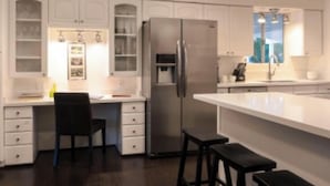 Een moderne keuken met witte kasten, een roestvrijstalen koelkast, een barkruk en een groot eiland.