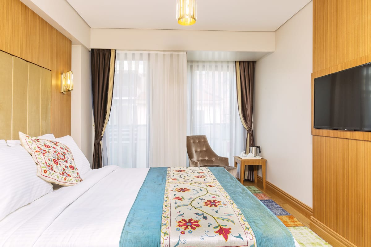 A hotel room with a bed, a chair, a television, and a small table with a lamp.
