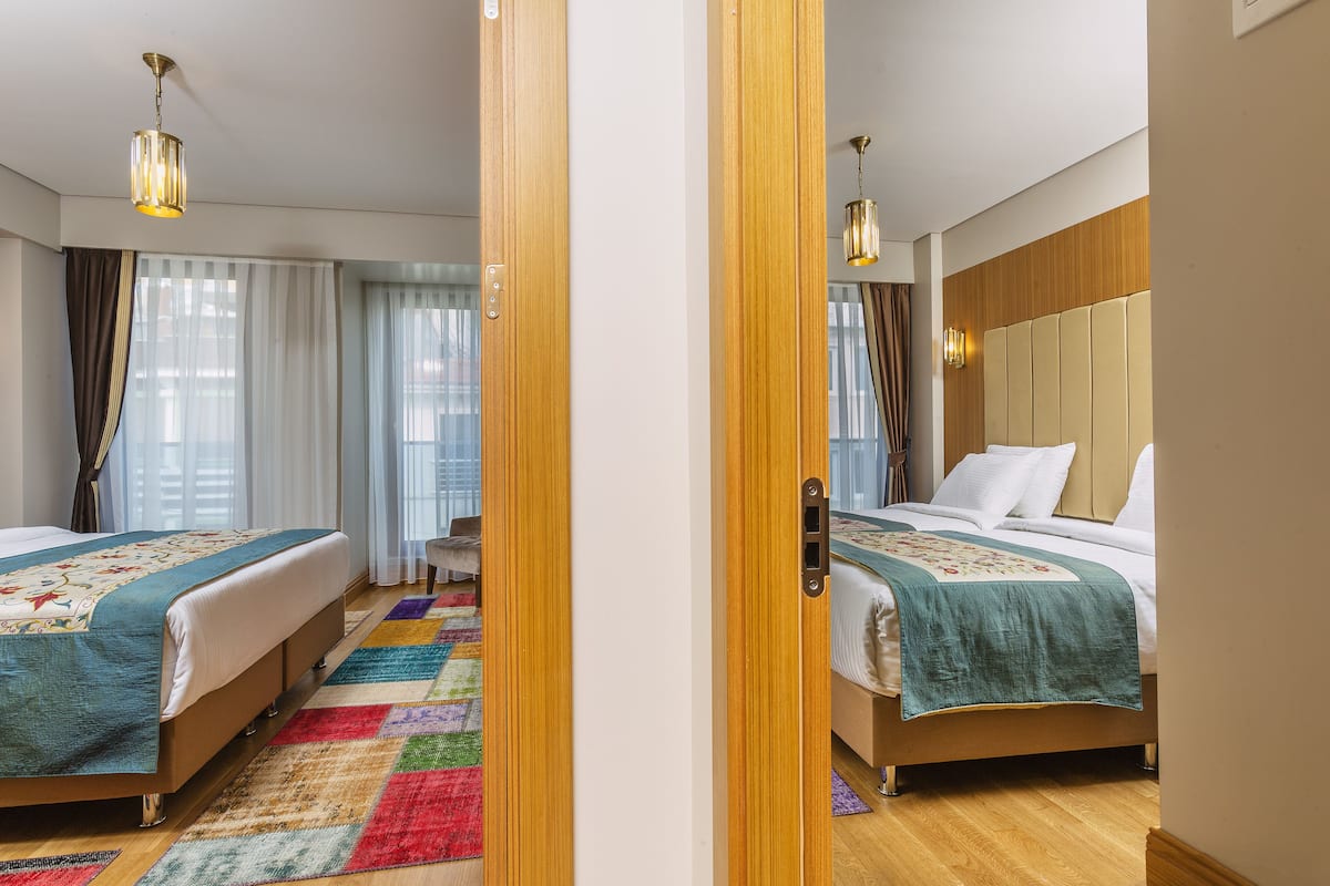 A hotel room with two beds, a colorful rug, wooden headboard, and a view of the city.