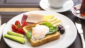 Un plato con tostadas, huevos, tomates, pepinos, aceitunas y queso, acompañado de una taza de café y té sobre una mesa.