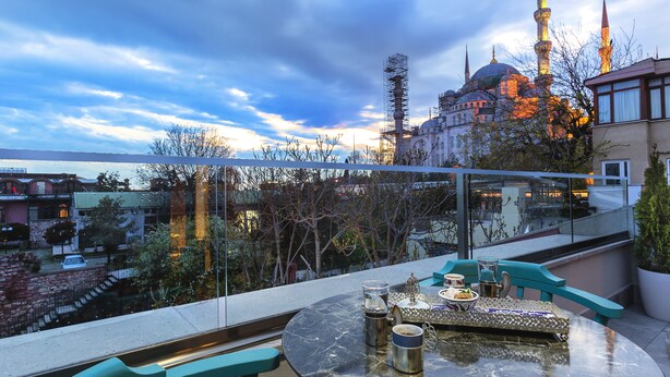 Una terraza con mesa dispuesta para comer, con vistas a un edificio histórico y un minarete destacado.