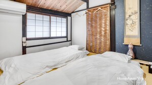 Ein Zimmer mit zwei Betten, einer Holzbalkendecke, einem Fenster und einem traditionellen japanischen Shoji-Bildschirm.