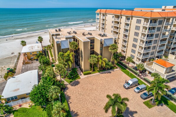 A beachfront hotel with multiple balconies, a sandy courtyard, and a view of the ocean.
