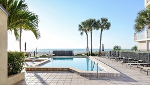Una piscina con vista al océano, rodeada de palmeras y mobiliario exterior.